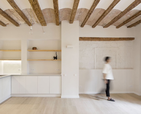 Interior de una vivienda con una cocian abierta al estar comedor, techo con bovedilla catalana, paviemento de parquet, y paredes y muebles color blanco